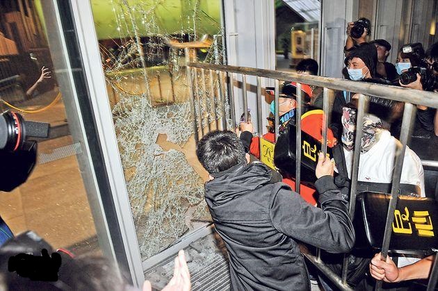 在立法會大樓外,多名蒙面男子合力抬起鐵馬,撞擊大樓出入口玻璃。